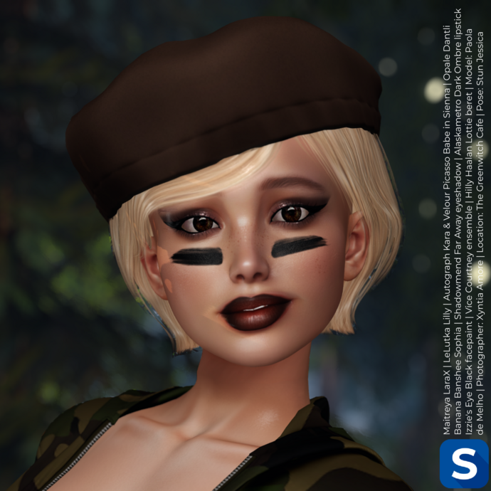 A headshot of Paola de Melho shows her standing in a forest while wearing a camp outfit. She has short blonde hair topped with a brown beret, while she has smoky eyeshadow, dark lipstick, and a black stripe of facepaint on each cheek.