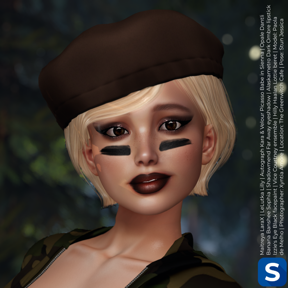 A headshot of Paola de Melho shows her standing in a forest while wearing a camp outfit. She has short blonde hair topped with a brown beret, while she has smoky eyeshadow, dark lipstick, and a black stripe of facepaint on each cheek.