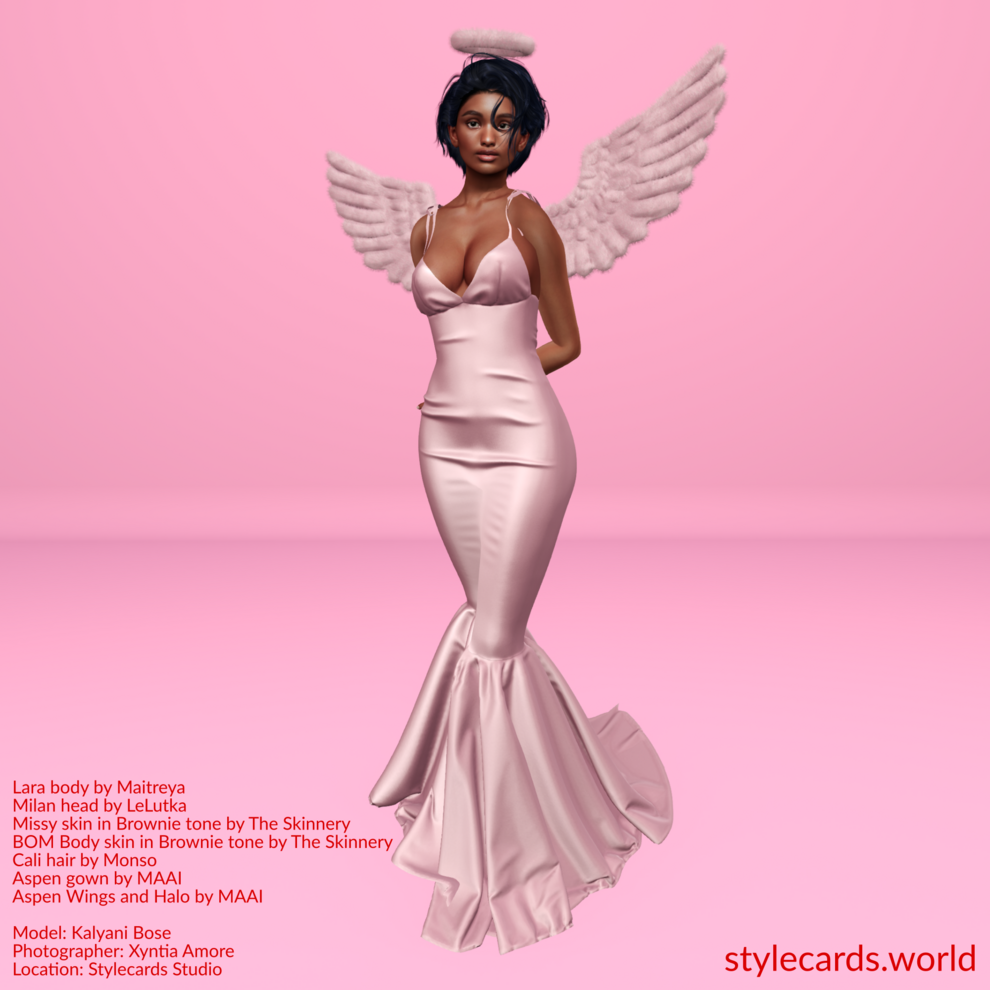 Kalyani Bose is dressed in a pink satin floor-length gown accessorized by a pink halo and angel wings while standing in front of a pink studio backdrop.