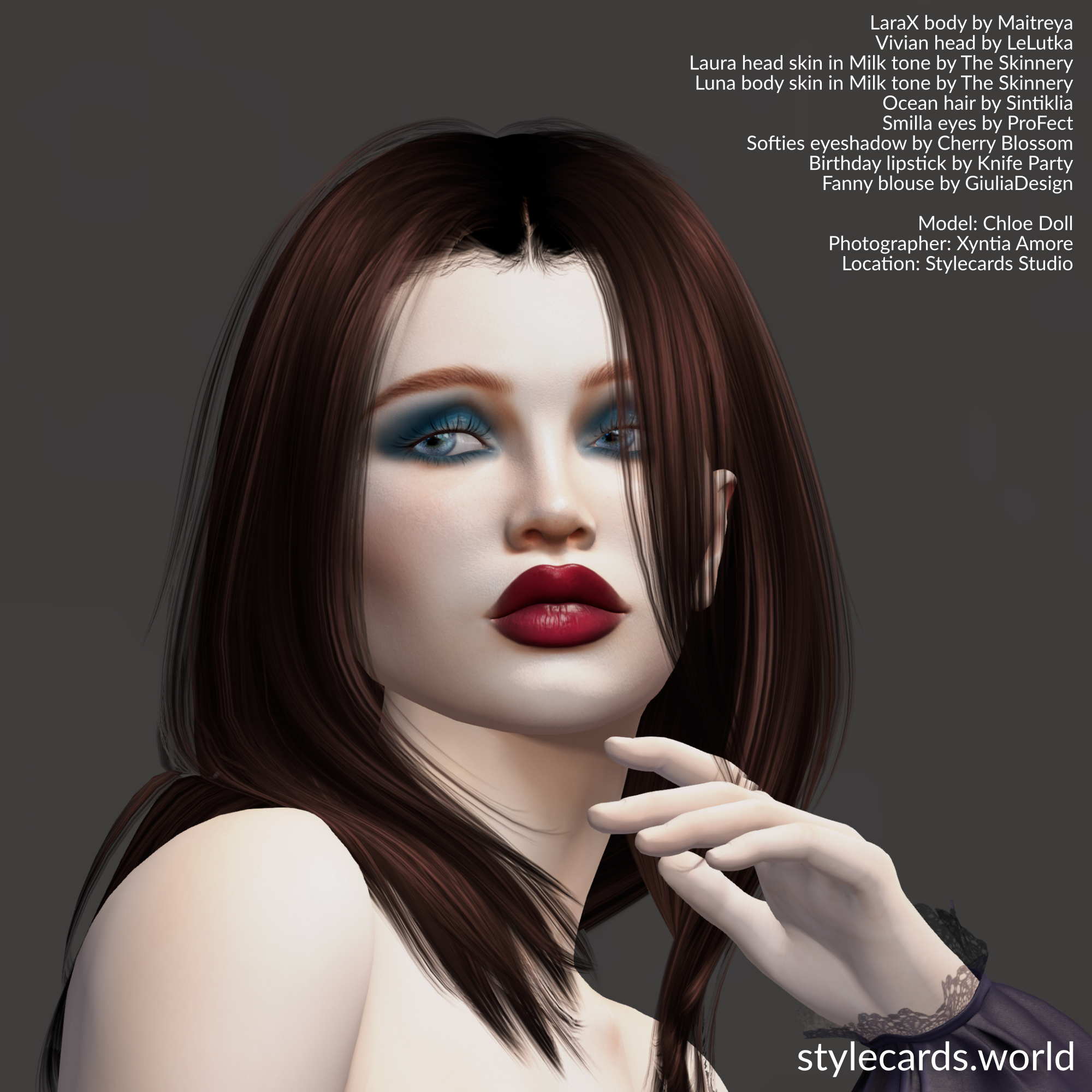 A headshot of Chloe Doll posing in front of a greay backdrop. She has long brown hair and is wearing bright red lipstick and dark turquoise eyeshadow.