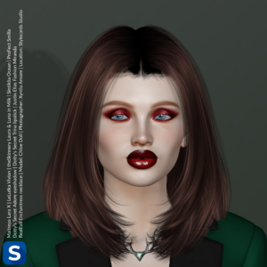 A headshot of model Chloe Doll standing in front of a grey-green backdrop. She is wearing a green tuxedo jacket with black lapels. Around her neck is a necklace inspired by the antlers of a deer. It is black metal and has a green gem in the center. Her hair is straight, brown, and reaches to her shoulders, while her lips are glistening dark red and match her dark red eyeshadow.