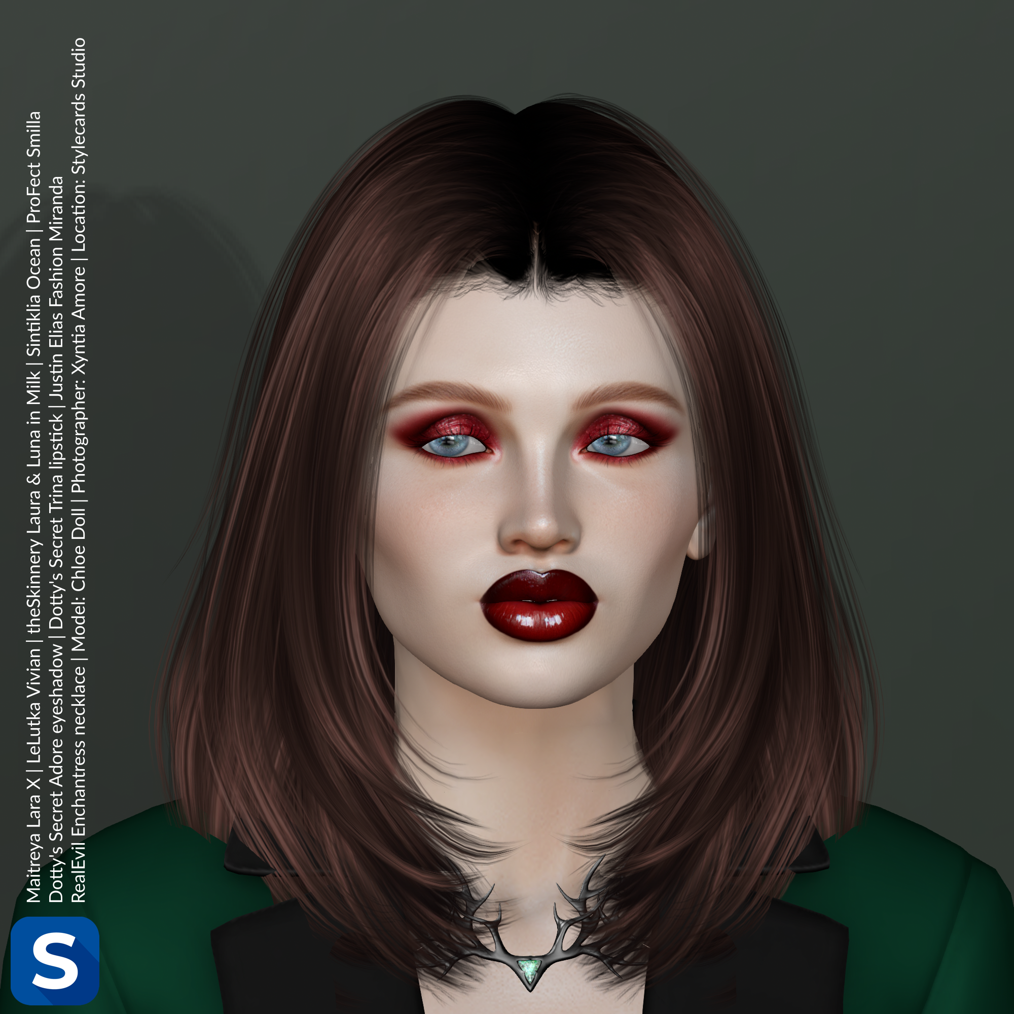 A headshot of model Chloe Doll standing in front of a grey-green backdrop. She is wearing a green tuxedo jacket with black lapels. Around her neck is a necklace inspired by the antlers of a deer. It is black metal and has a green gem in the center. Her hair is straight, brown, and reaches to her shoulders, while her lips are glistening dark red and match her dark red eyeshadow.