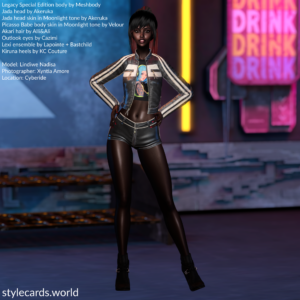 Lindiwe Nadisa is standing in front of some neon signs while wearing black leather shorts, a t-shirt, and a black leather jacket with white stripes running down the arms. She is standing with her hands on her hips and she is smiling for the camera.