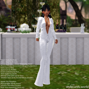 Tala Pangilinan is wearing a white leather suit that's accessorized with a gold and pearl earring and necklace set. She is posing at an outdoor wedding venue in front of a banquet table adorned with flower arrangements and bottles of champagne.