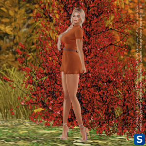 A full-length photo of Ivy Qissentell wearing an orange minidress while posed in front of some autumnal foliage. She has long blonde hair and is wearing high heels.
