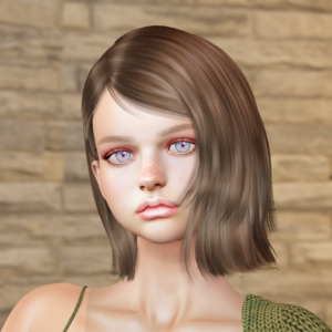A headshot of a model standing in front of a wall made of beige bricks. She has short brown hair and her shoulders are draped with an olive green sweater. Her lips are sealed with pale pink lipstick, while her eyelids are adorned with pink eyeshadow and her nose features a flock of freckles.