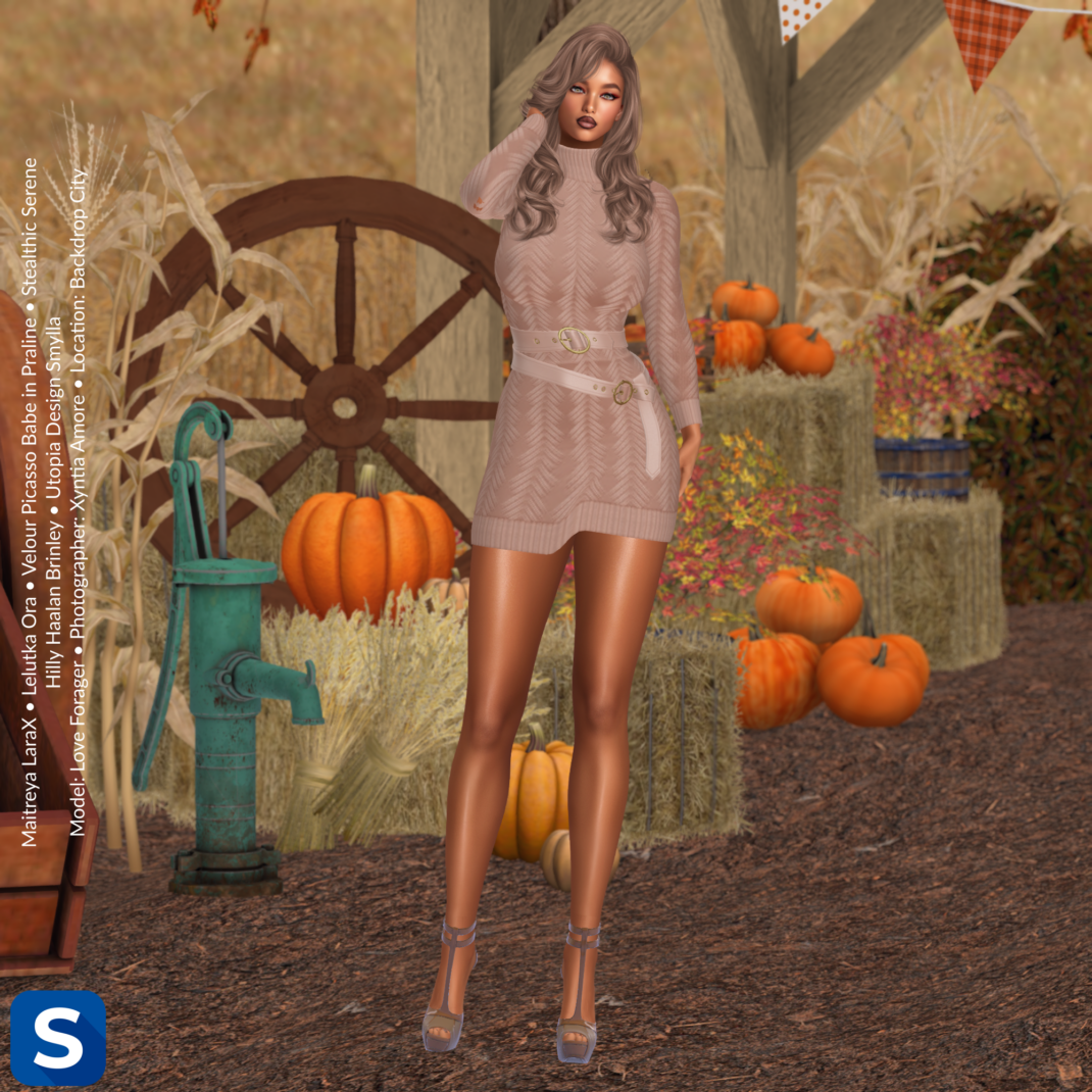 Threadsday, August 27, 2026 In a barnyard with hay bales and pumpkins in the background behind her, our model wears a light brown belted sweaterdress and high heels. Her long wavy hair is a color similar to the dress.