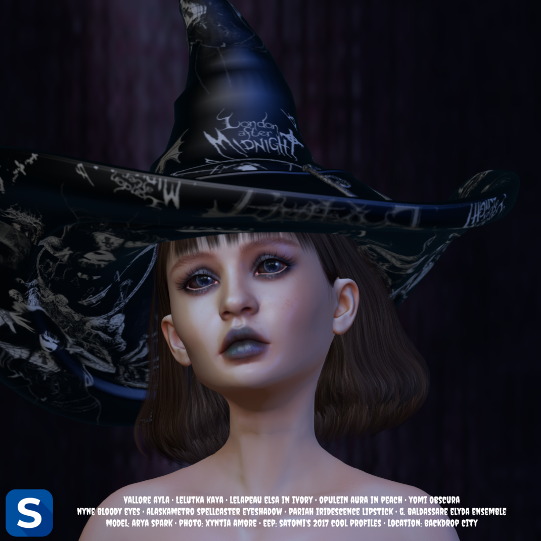 Makeup Monday, October 5, 2026 A headshot of a woman with a black witch's hat perched upon her head as she is standing in front of a darkened backdrop. The scleras and irises of her eyes are blackened as if she is cursed by a dark magic. Her eyeshadow and lipstick are both a dark ghoulish grey.